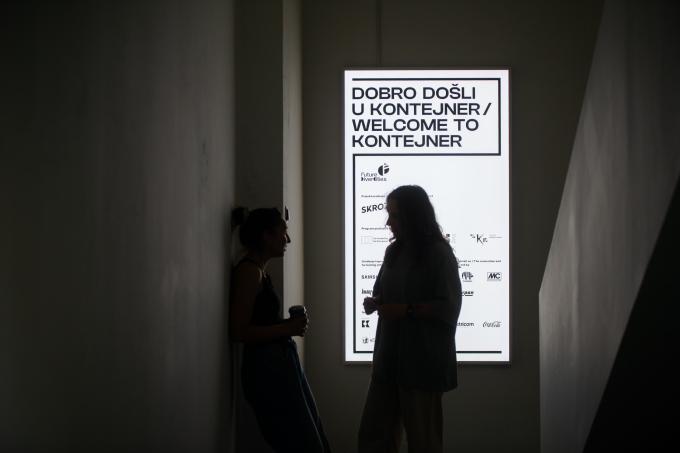 Silhouette of two persons talking in a dark hallway with a bright sign in the back